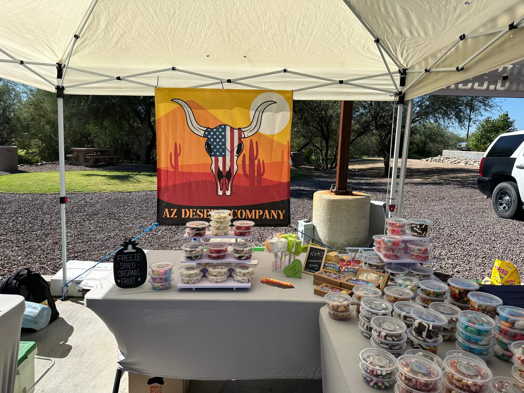 Outdoor event with a table displaying products under a tent featuring an AZ Desert Company banner.