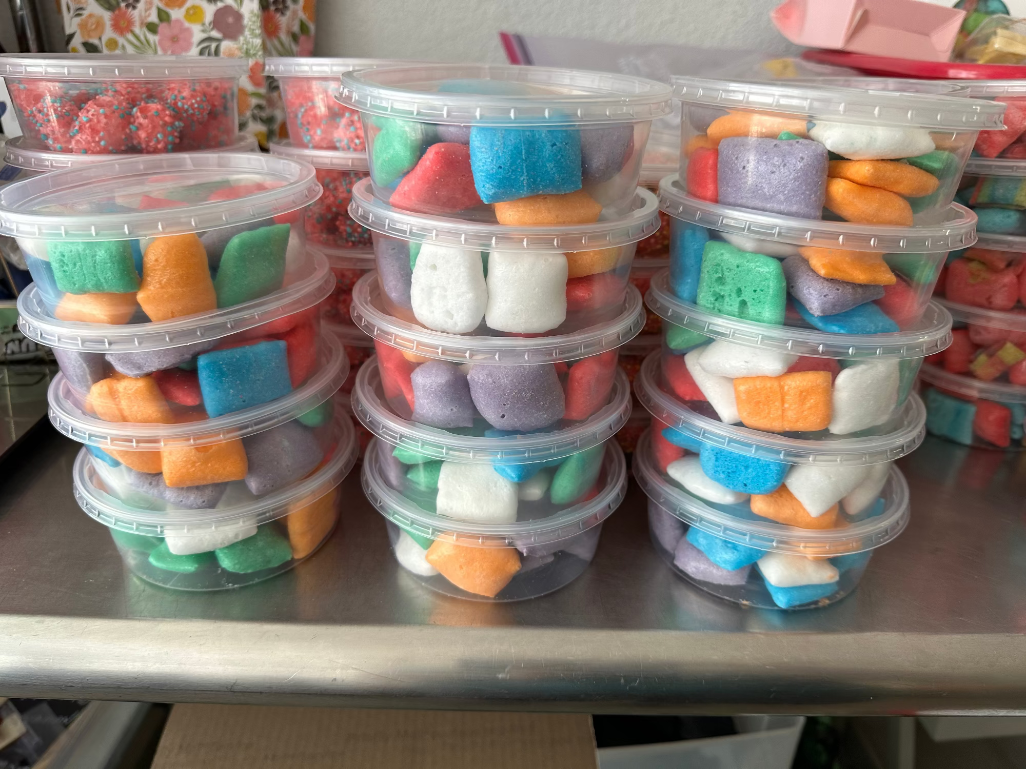 Stacks of colorful freeze dried airheadz in clear plastic containers on a metal surface.