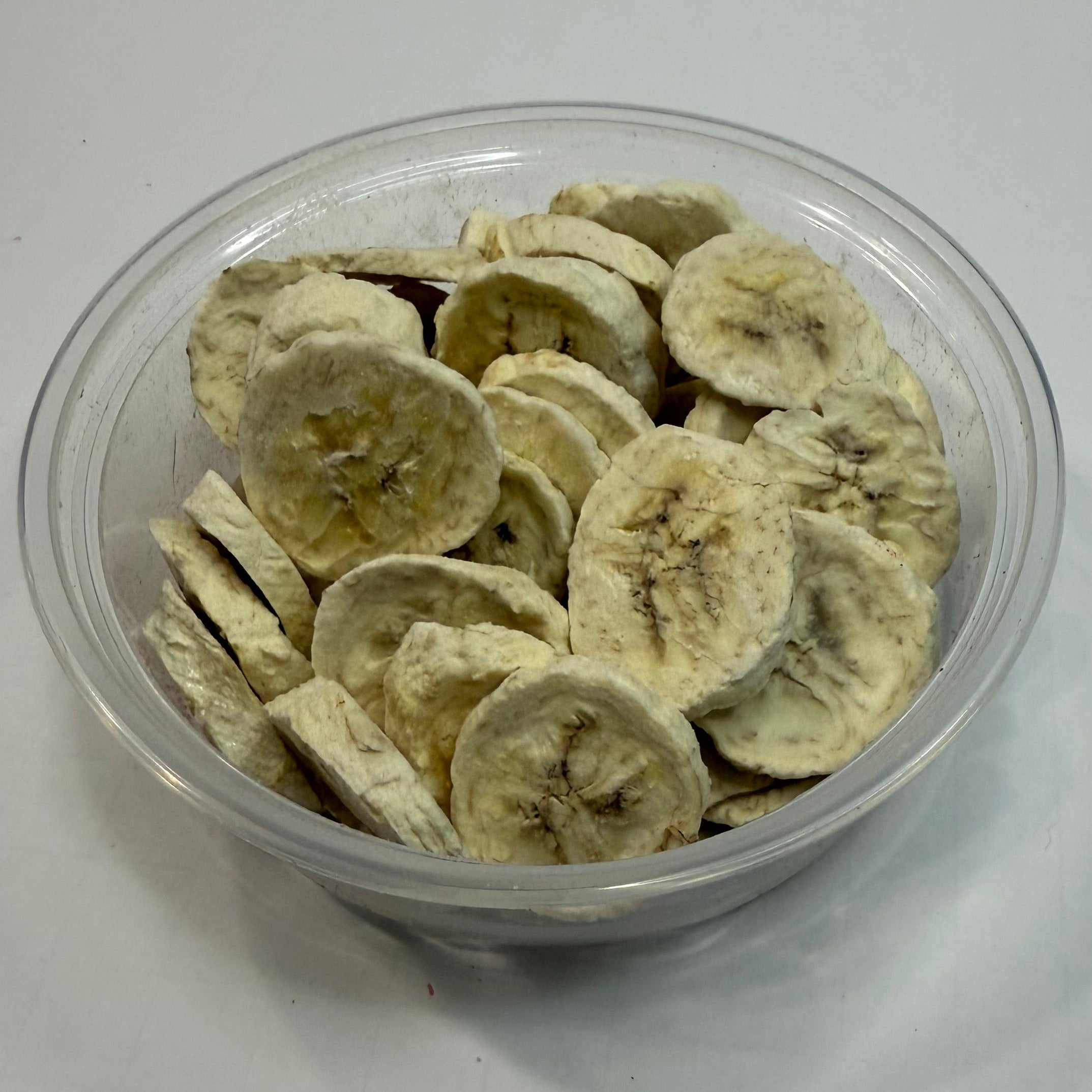 Clear plastic container filled with sliced freeze dried bananas on a white background