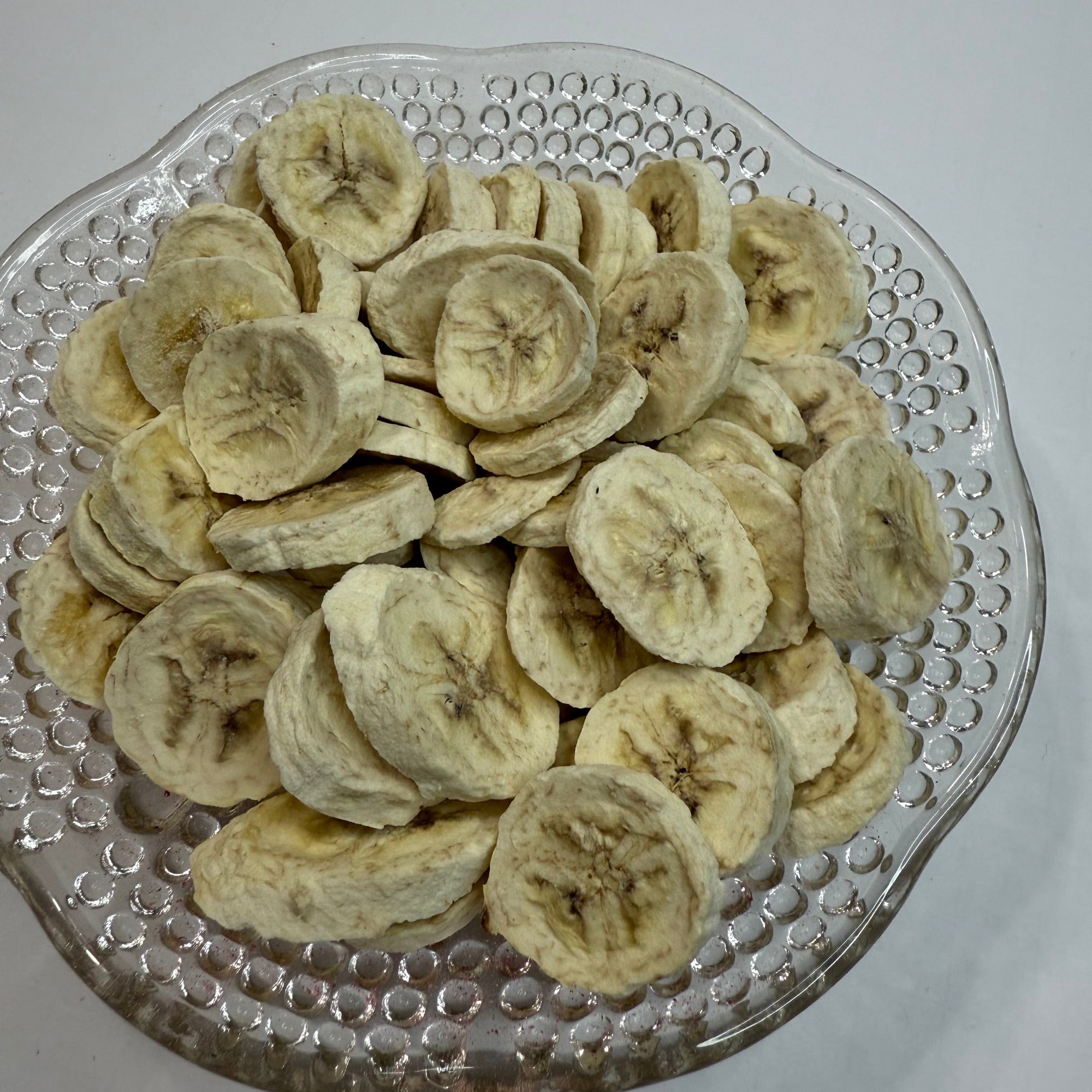 Freeze dried banana slices on a decorative glass plate with a plain background