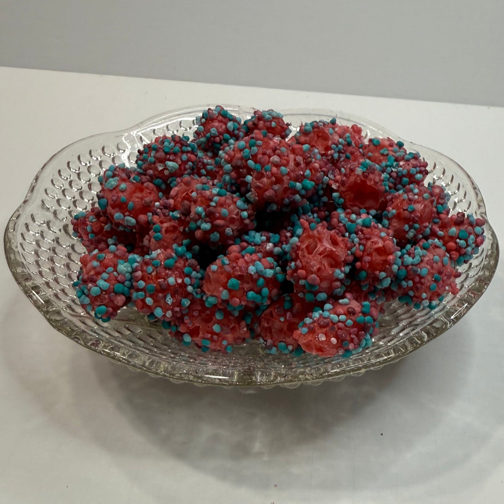 Decorative glass bowl with freeze dried berry blue nerds gummy clusters on a white surface