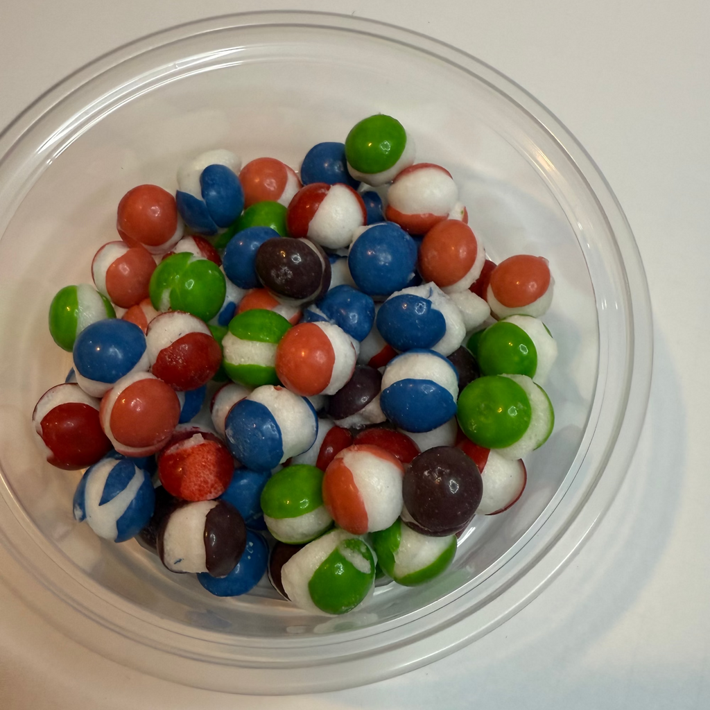 Clear plastic container filled with freeze dried berry skittles on a white surface