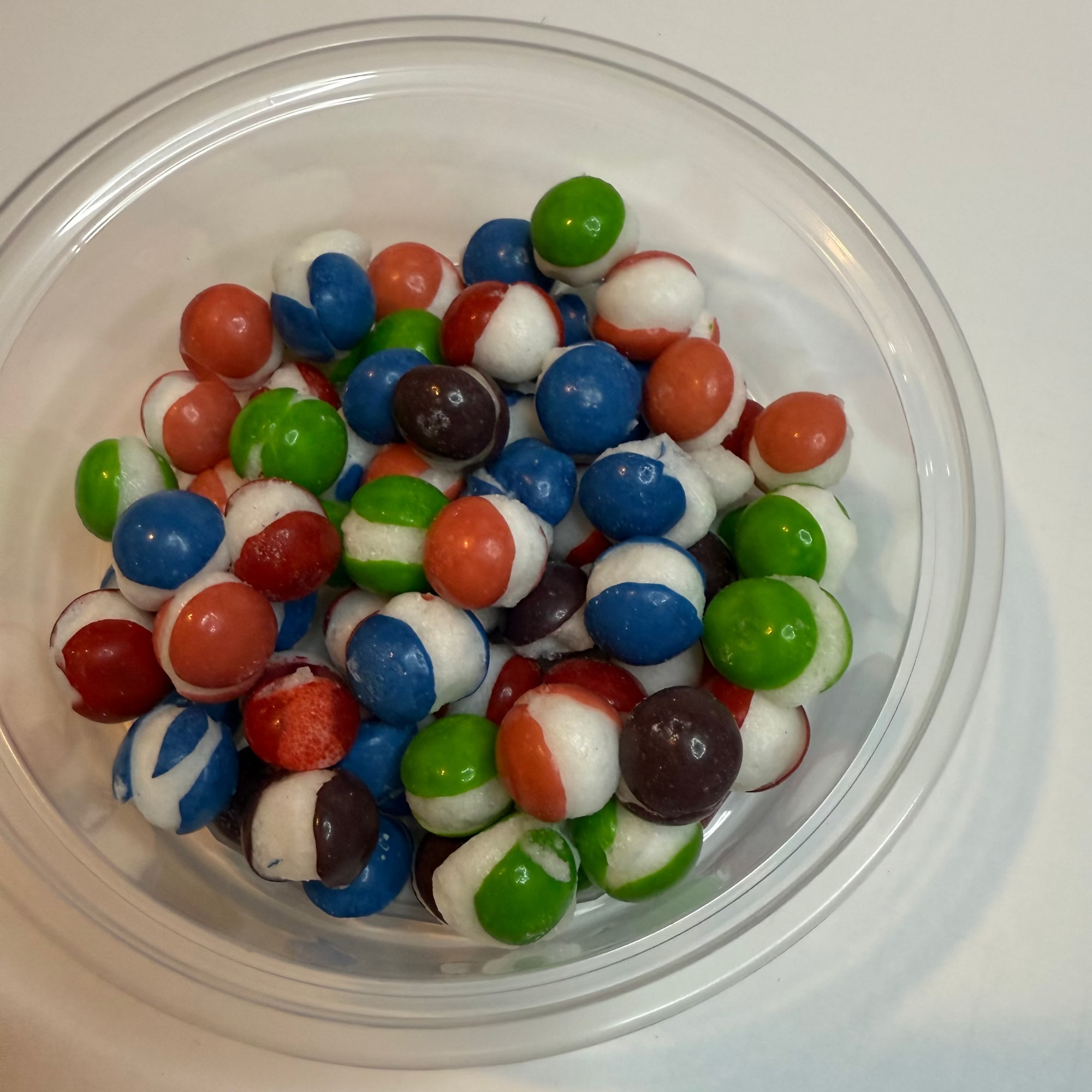 Clear plastic container filled with freeze dried berry skittles on a white surface