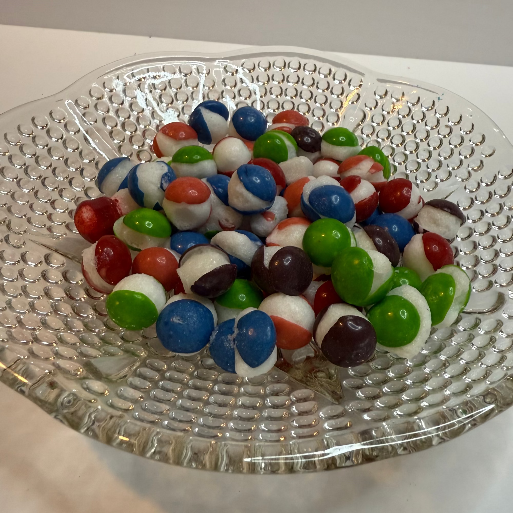 Freeze dried berry skittles on a clear glass plate with a white background