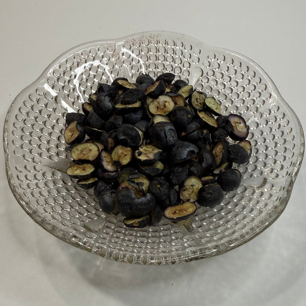 Clear glass strainer with freeze dried blueberries on a white surface