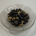 Clear glass strainer with freeze dried blueberries on a white surface