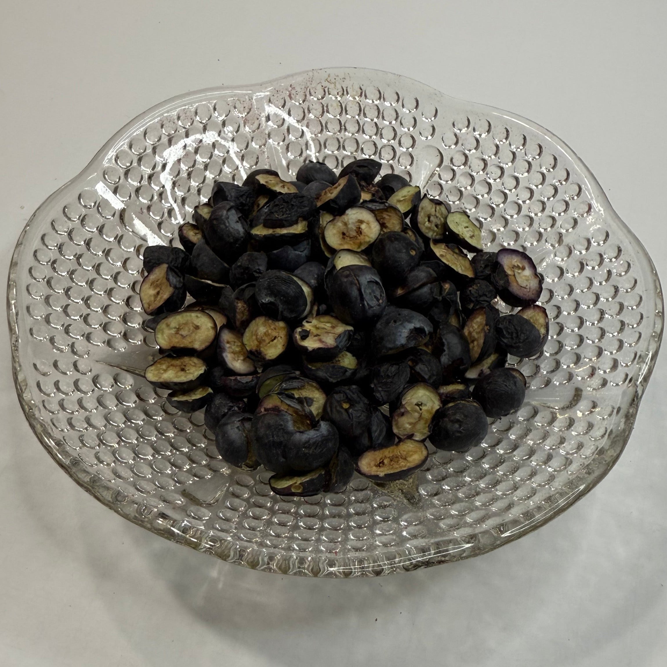 Clear glass strainer with freeze dried blueberries on a white surface