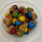 Clear container with freeze dried caramel M&M candies on a white background