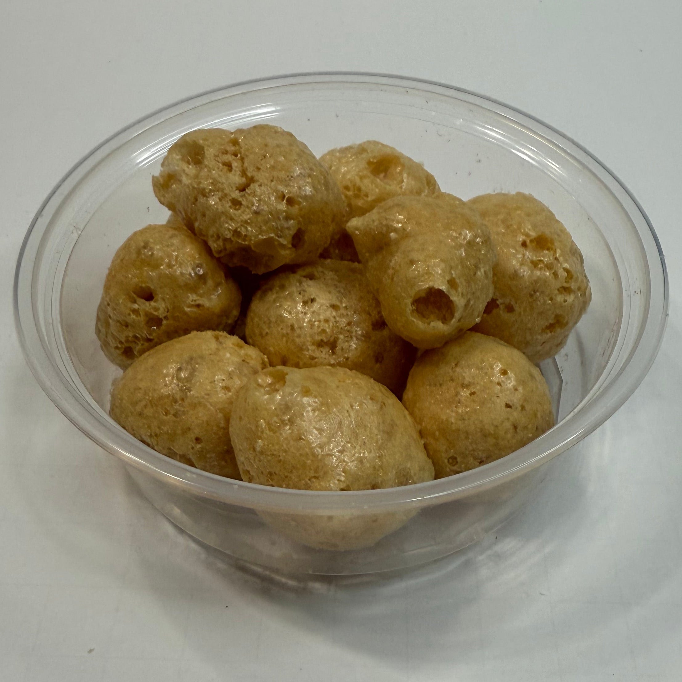 Clear plastic cup filled with freeze dried caramels on a white background