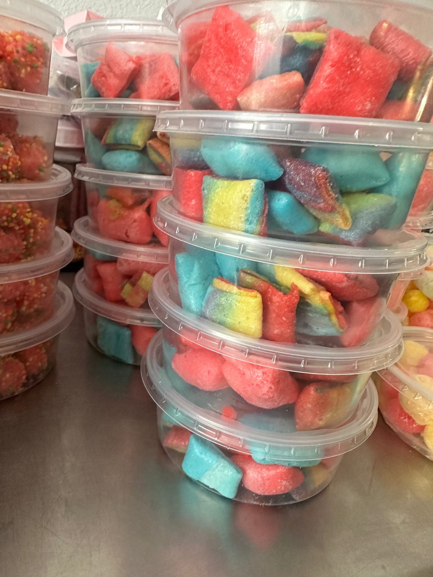 Stacks of clear plastic containers filled with colorful freeze dried candies on a metal surface.