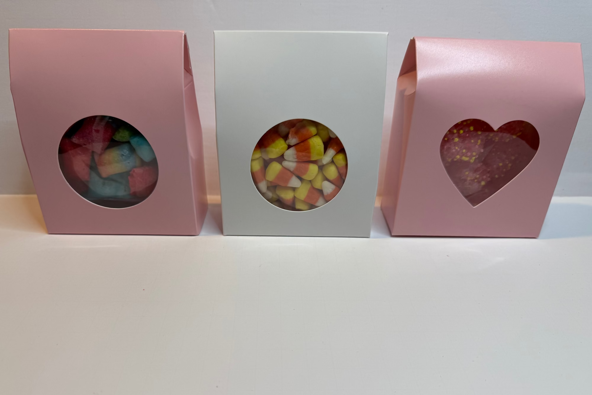 Three small gift boxes with windowed tops and a heart design on a white background