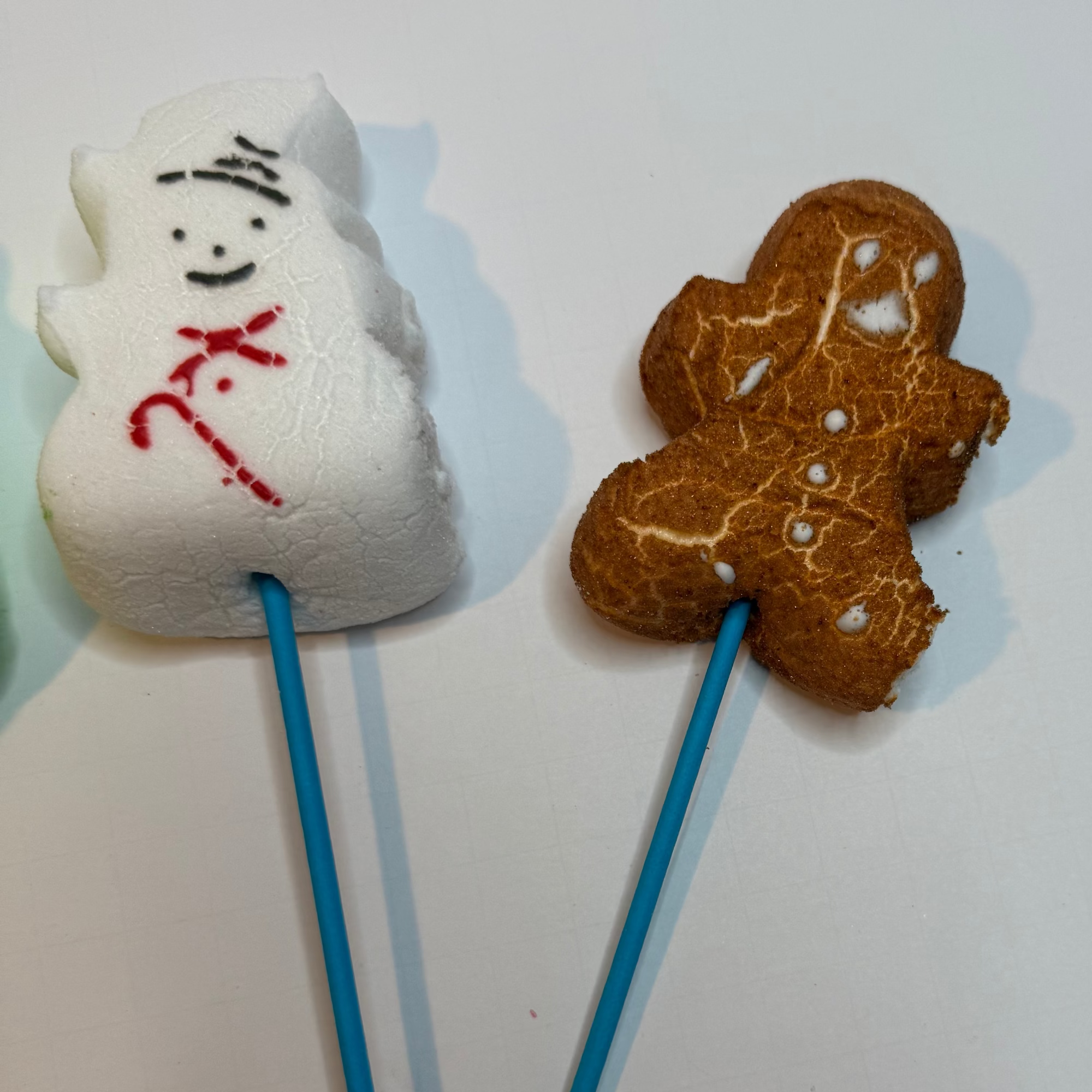 Freeze dried snowman and gingerbread man peeps on sticks against a white background