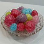 Colorful freeze dried jolly ranchers in a clear glass container on a white background