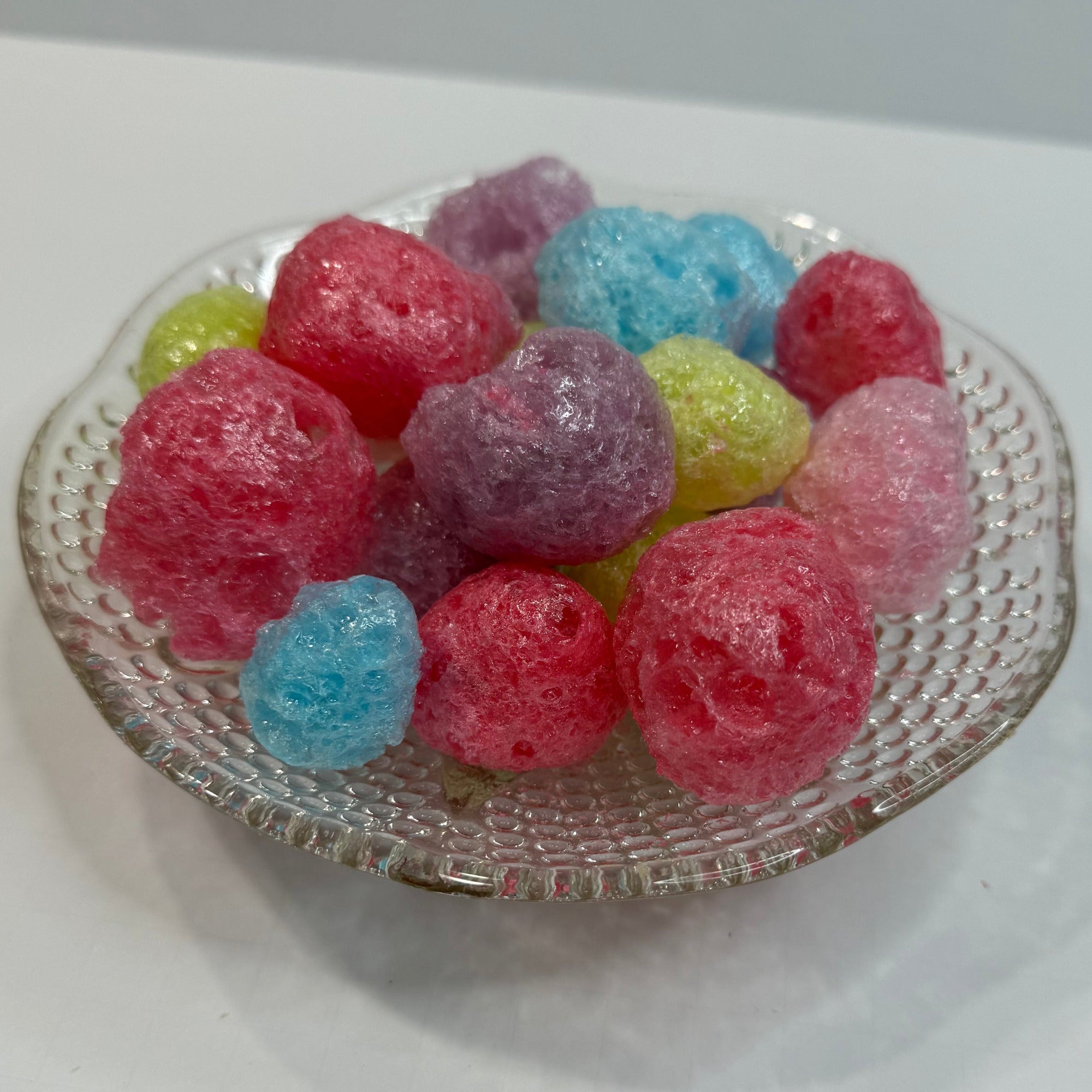Colorful freeze dried jolly ranchers in a clear glass container on a white background