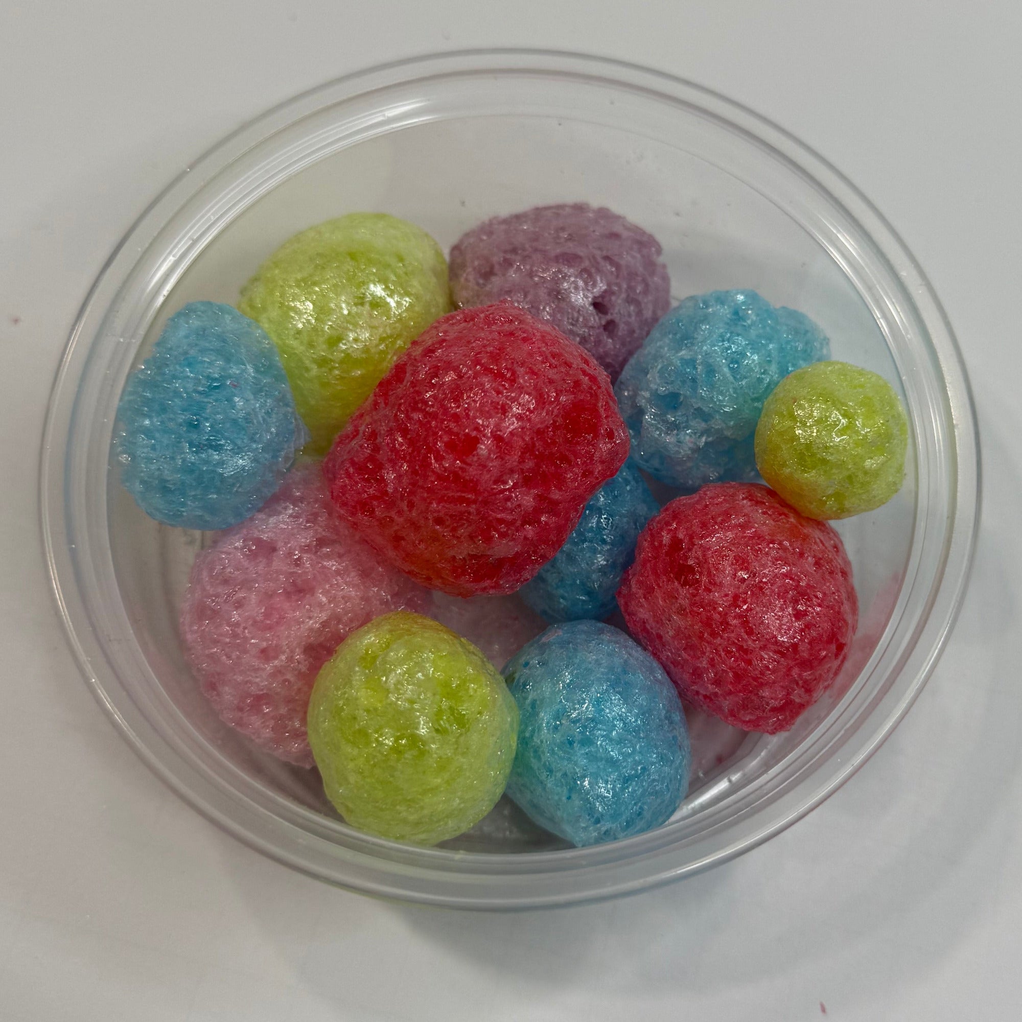 Clear plastic container with freeze dried jolly ranchers on a white surface