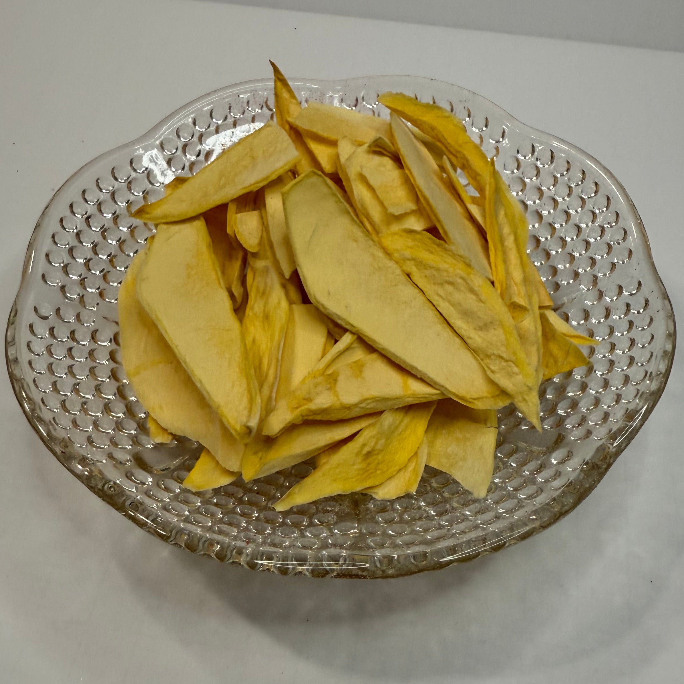 Clear glass plate with freeze dried mango slices on a white surface