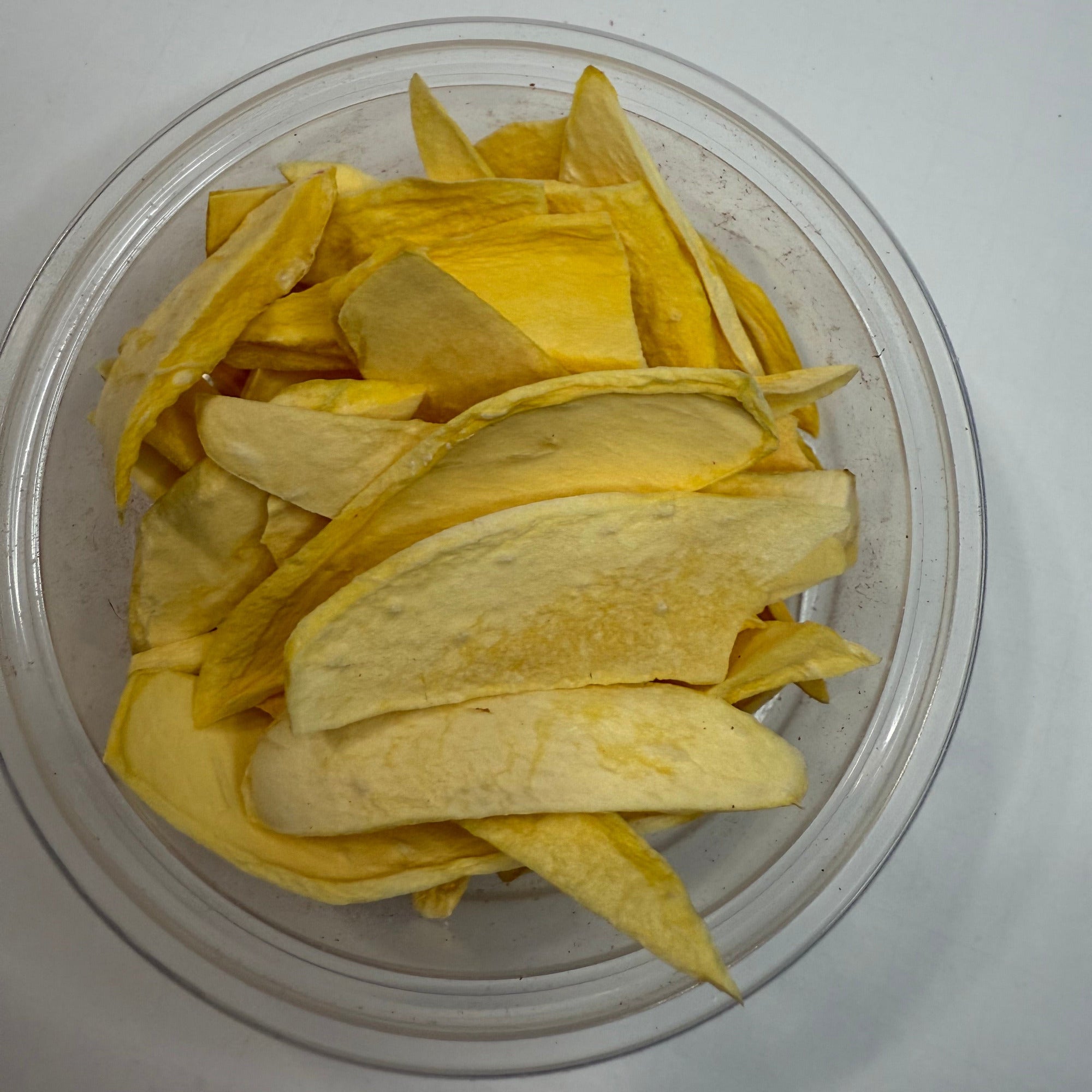 Clear container with sliced freeze dried mango on a white background