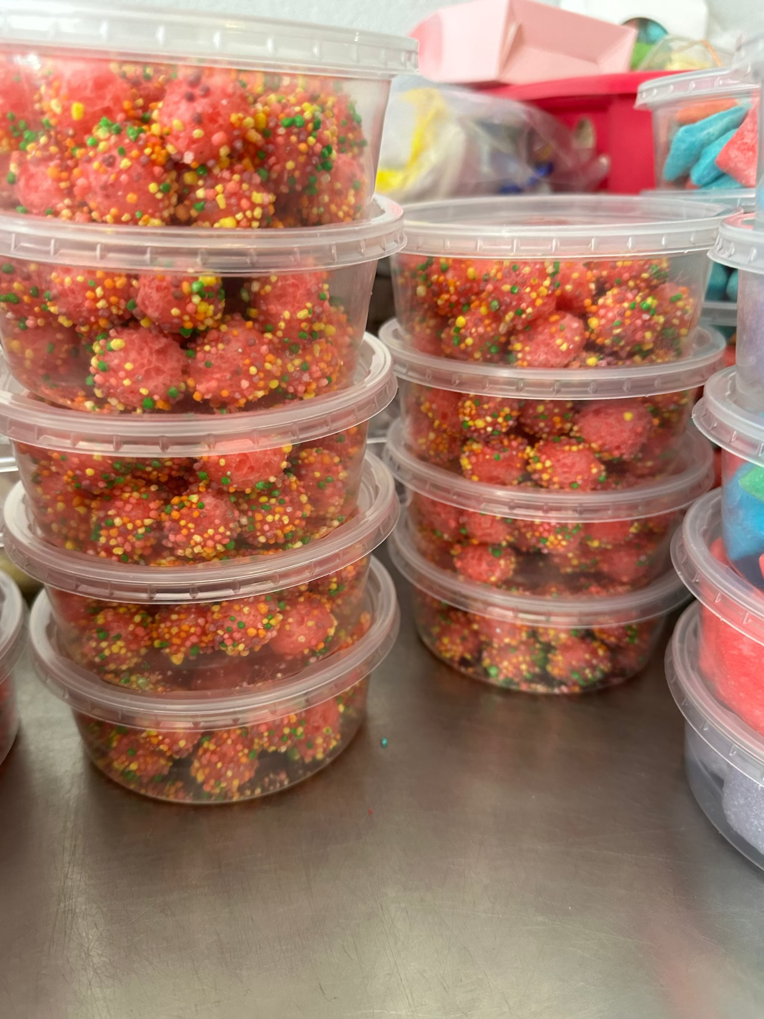 Stacks of containers filled with colorful freeze dried nerdz gummy clusters on a metal surface.