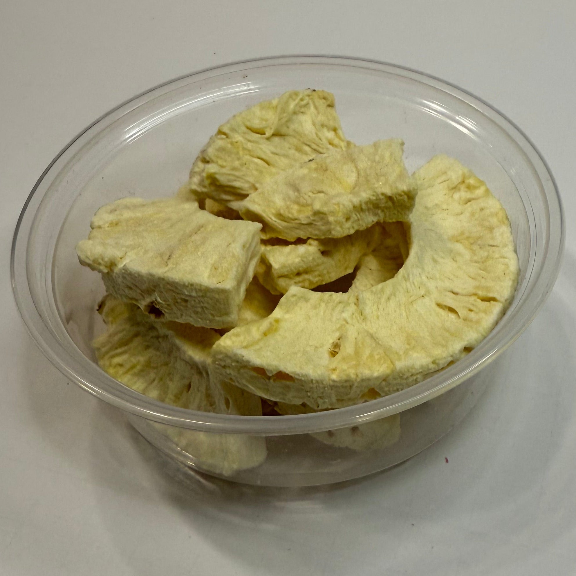 Clear plastic container with freeze dried pineapple on a white background