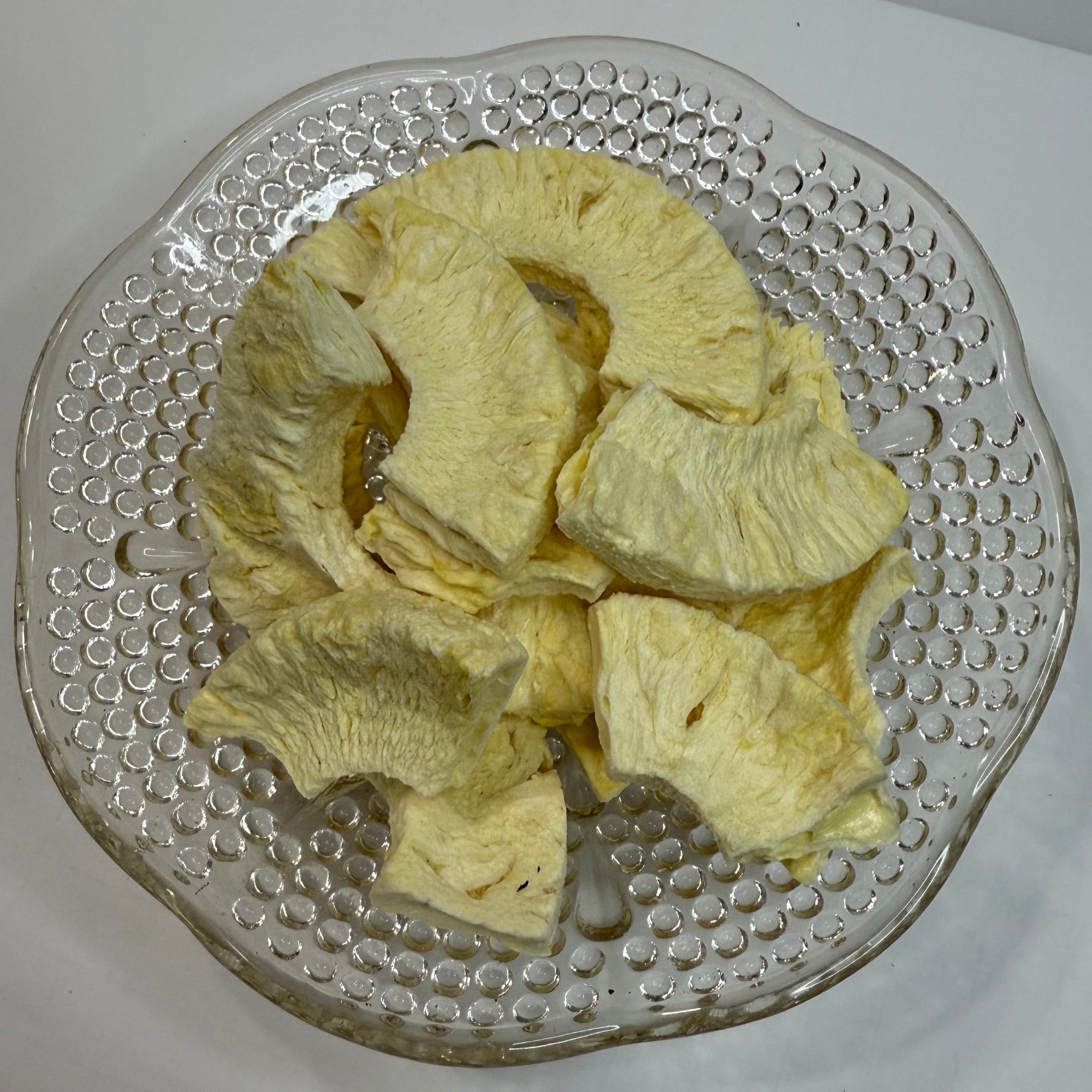 Freeze dried pineapple slices on a textured glass plate with a white background