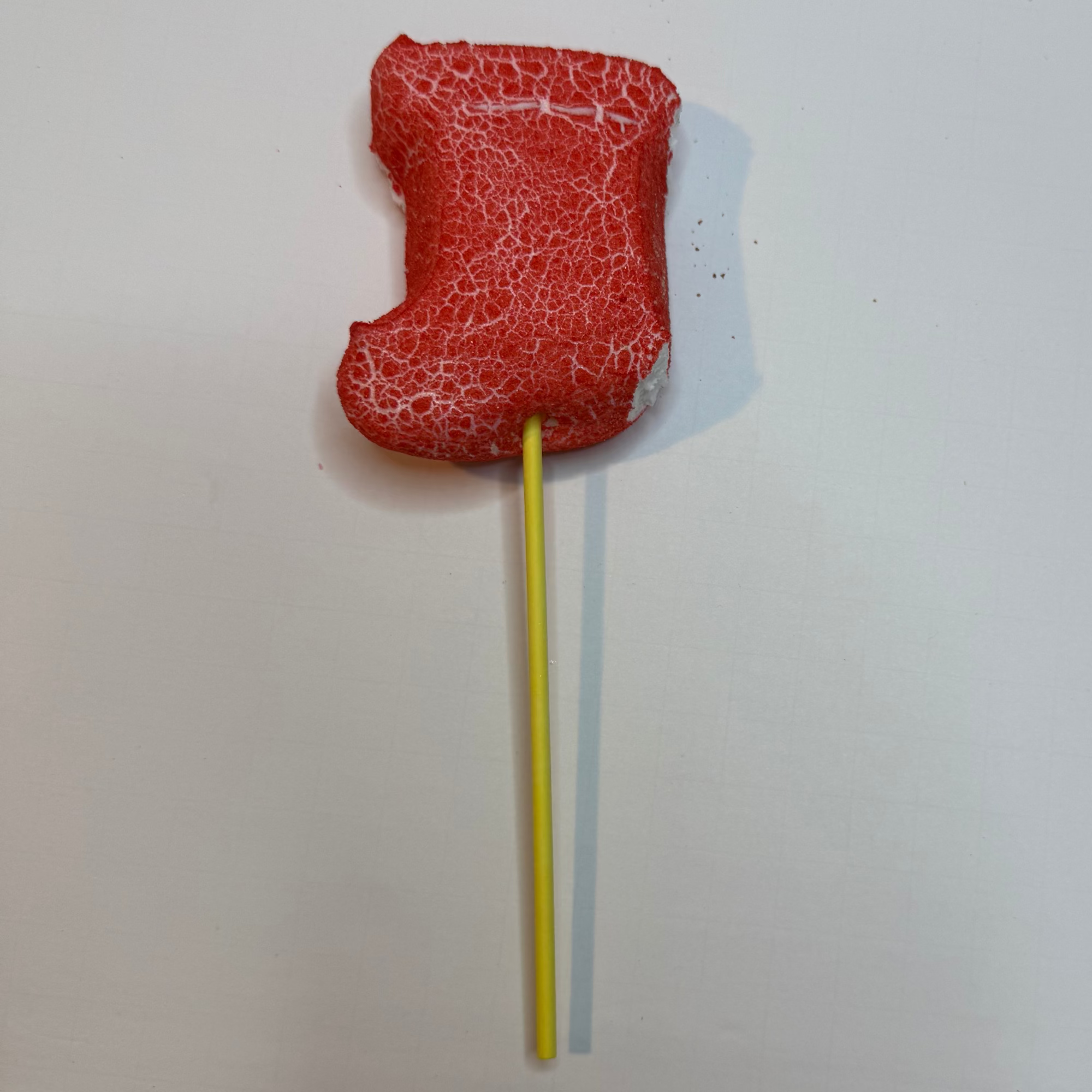 Freeze dried red stocking peep with a yellow stick on a white background