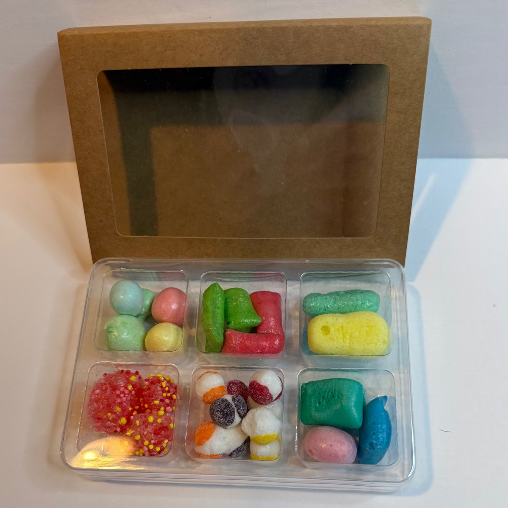 Assorted colorful candies in a clear plastic container with a brown cardboard box on a white surface.