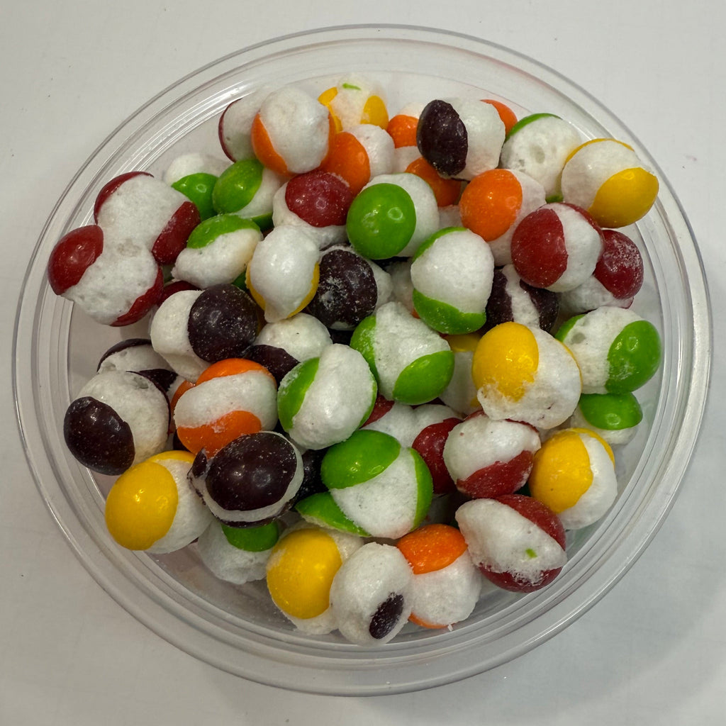 Freeze dried skittles in a clear plastic container on a white background