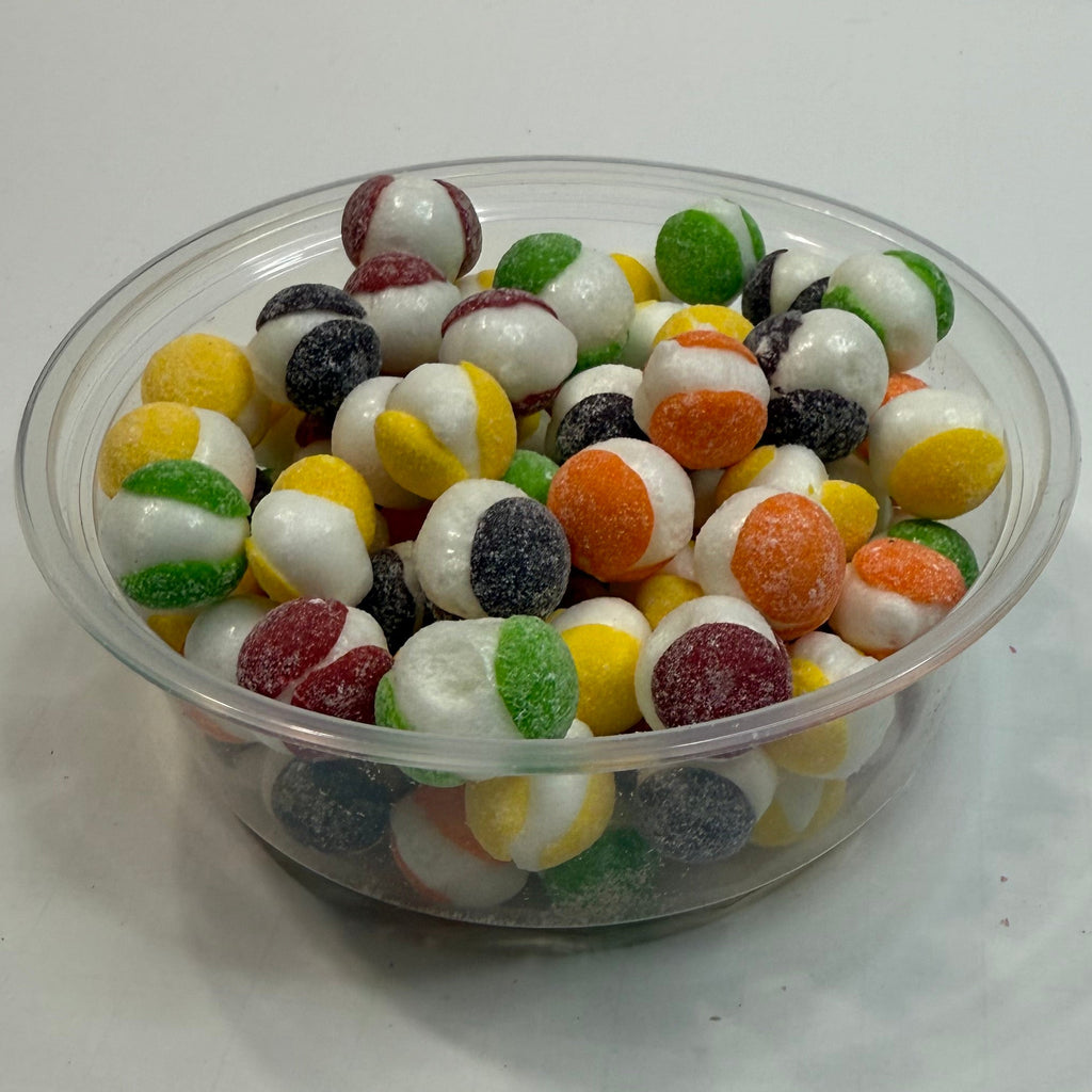 Clear plastic container filled with freeze dried sour skittles on a white surface