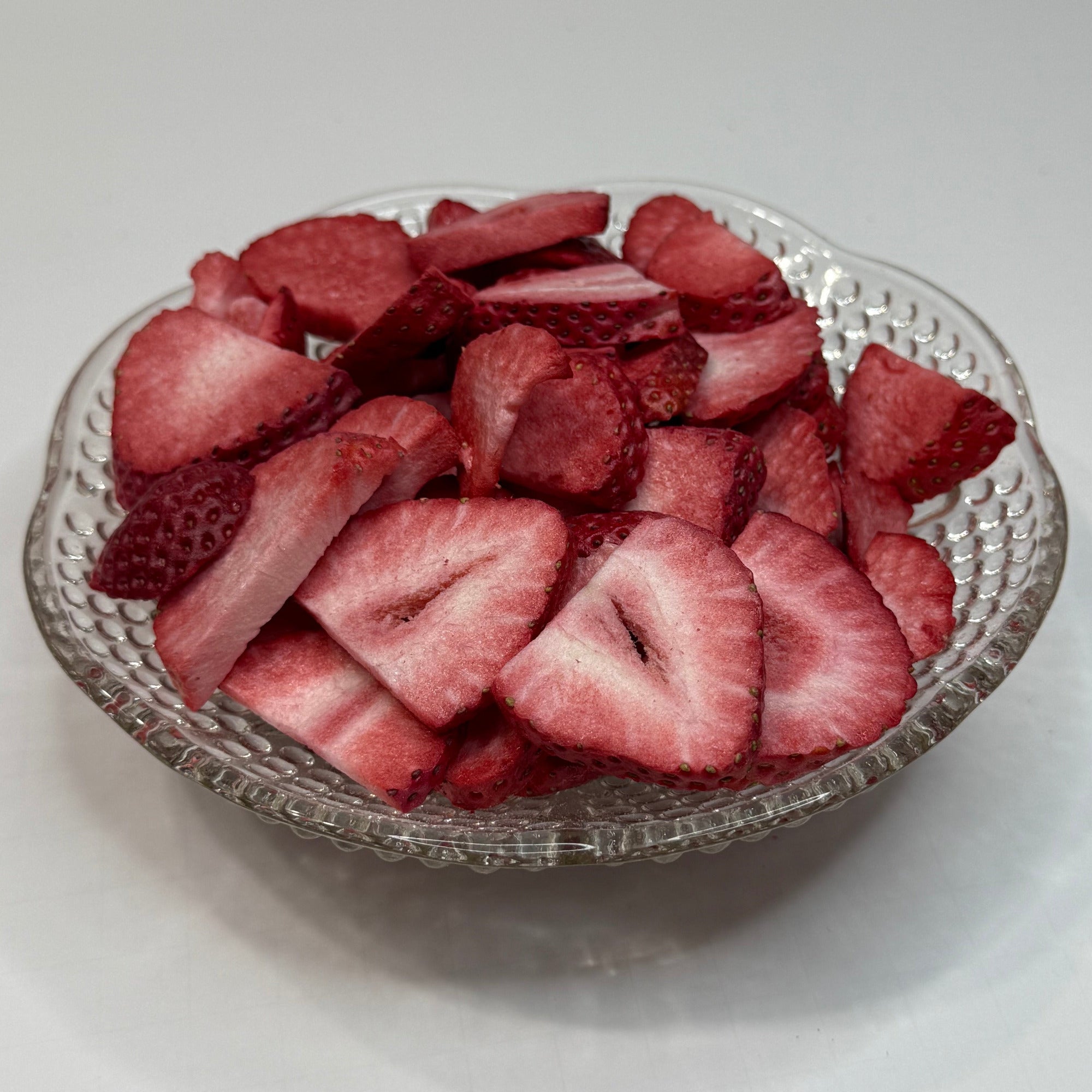 Sliced freeze dried strawberries in a decorative glass bowl on a white background