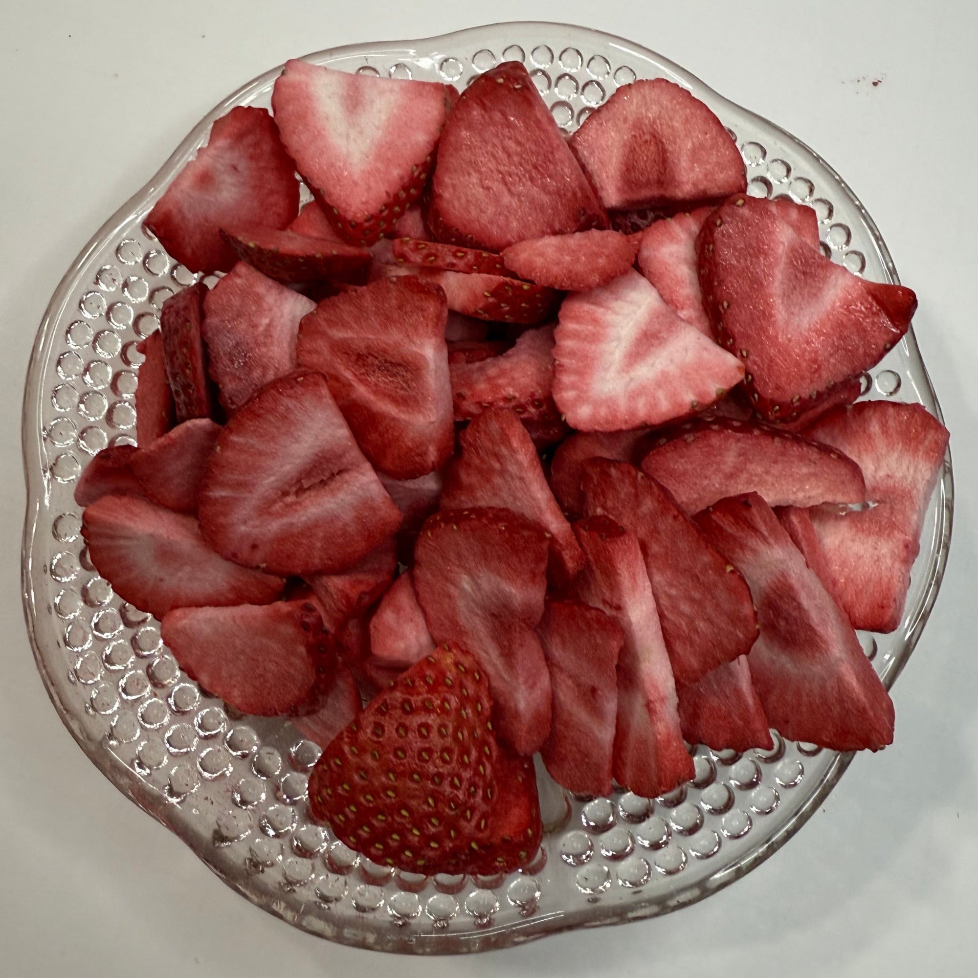 Sliced freeze dried strawberries on a decorative glass plate with a plain background