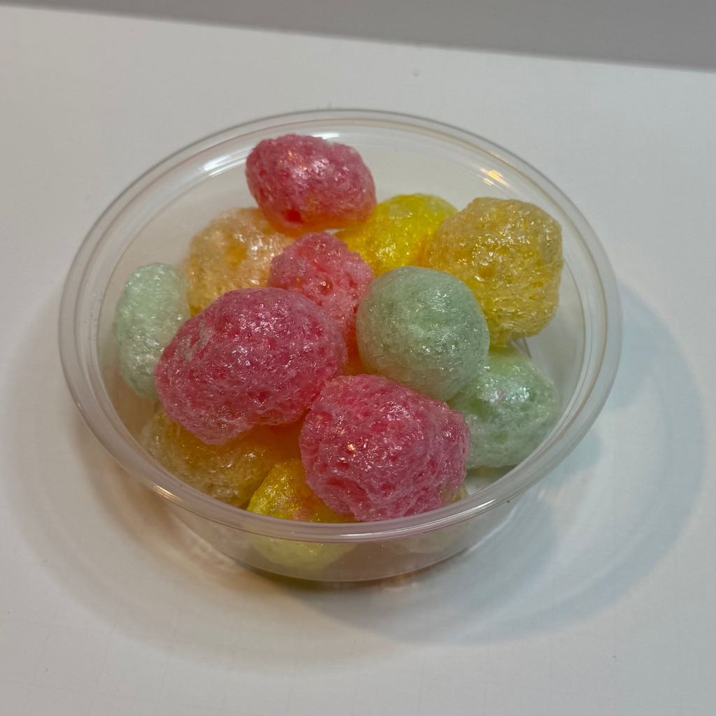 Clear plastic cup filled with freeze dried tropical jolly ranchers on a white surface