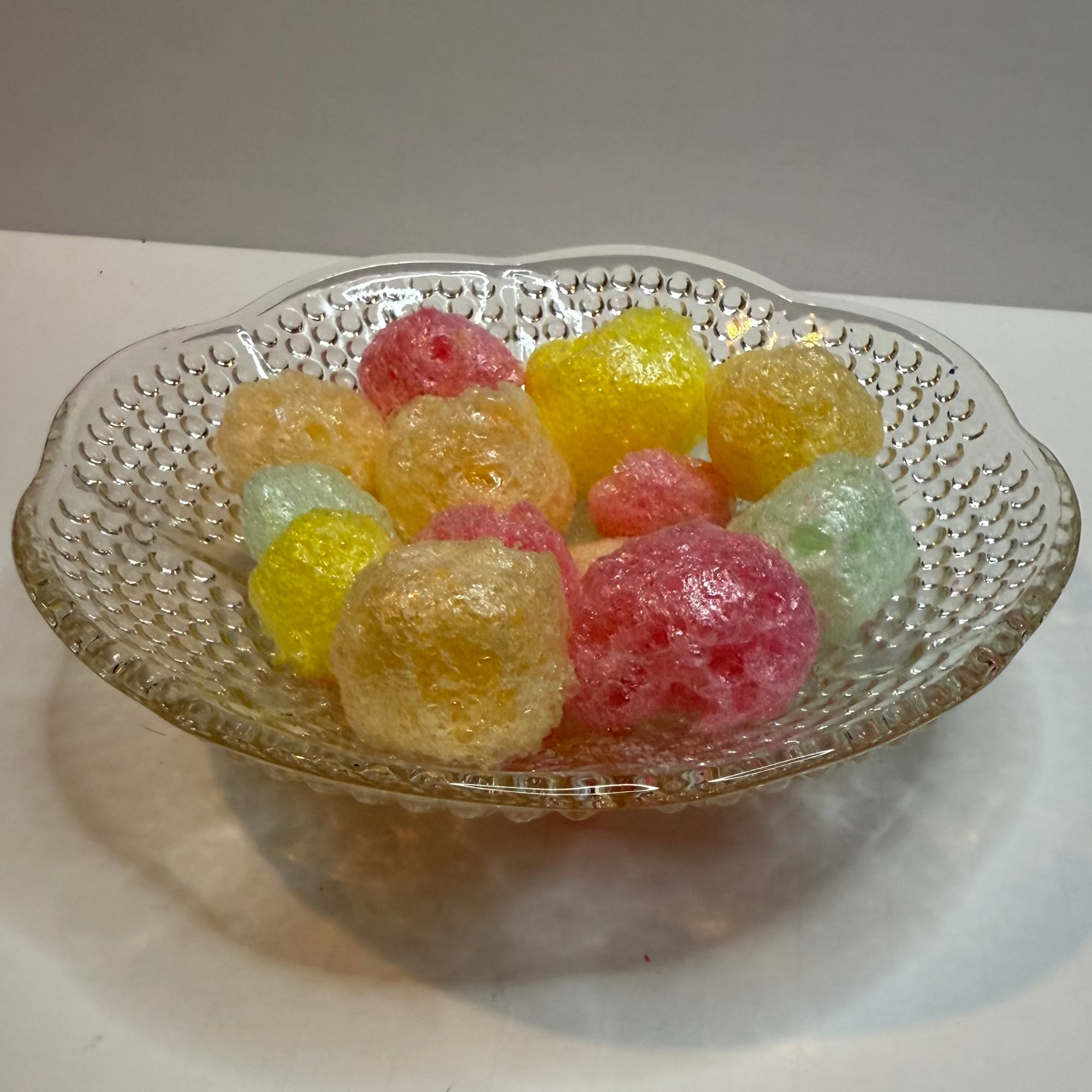 Decorative glass bowl filled with colorful freeze dried tropical jolly ranchers on a white surface