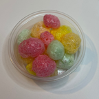 Clear container with freeze dried tropical jolly ranchers on a white surface