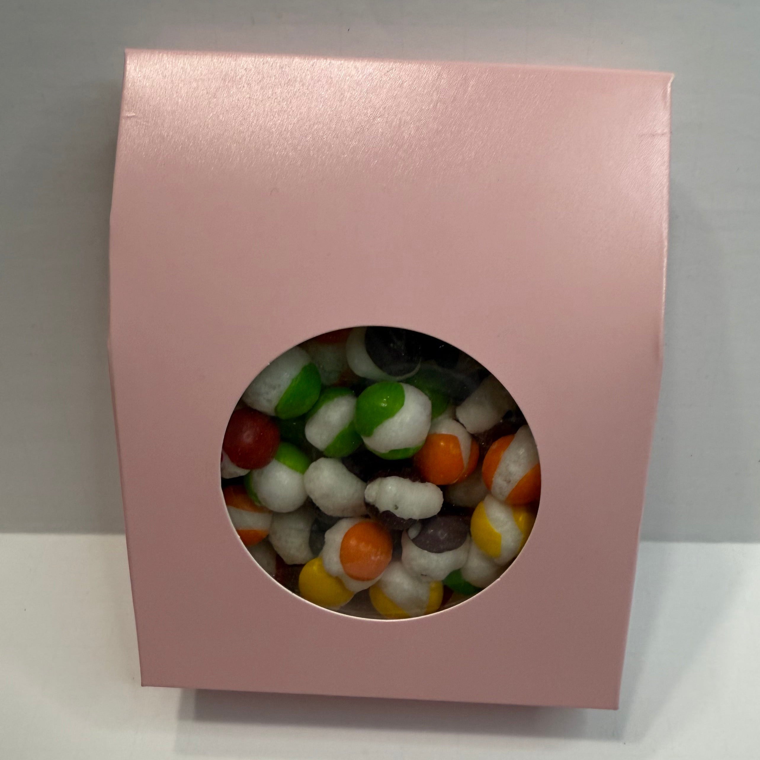 Pink box with a window displaying freeze dried skittles on a gray background