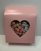 Pink box with a heart-shaped window displaying colorful freeze dried marshmallow charms on a white background