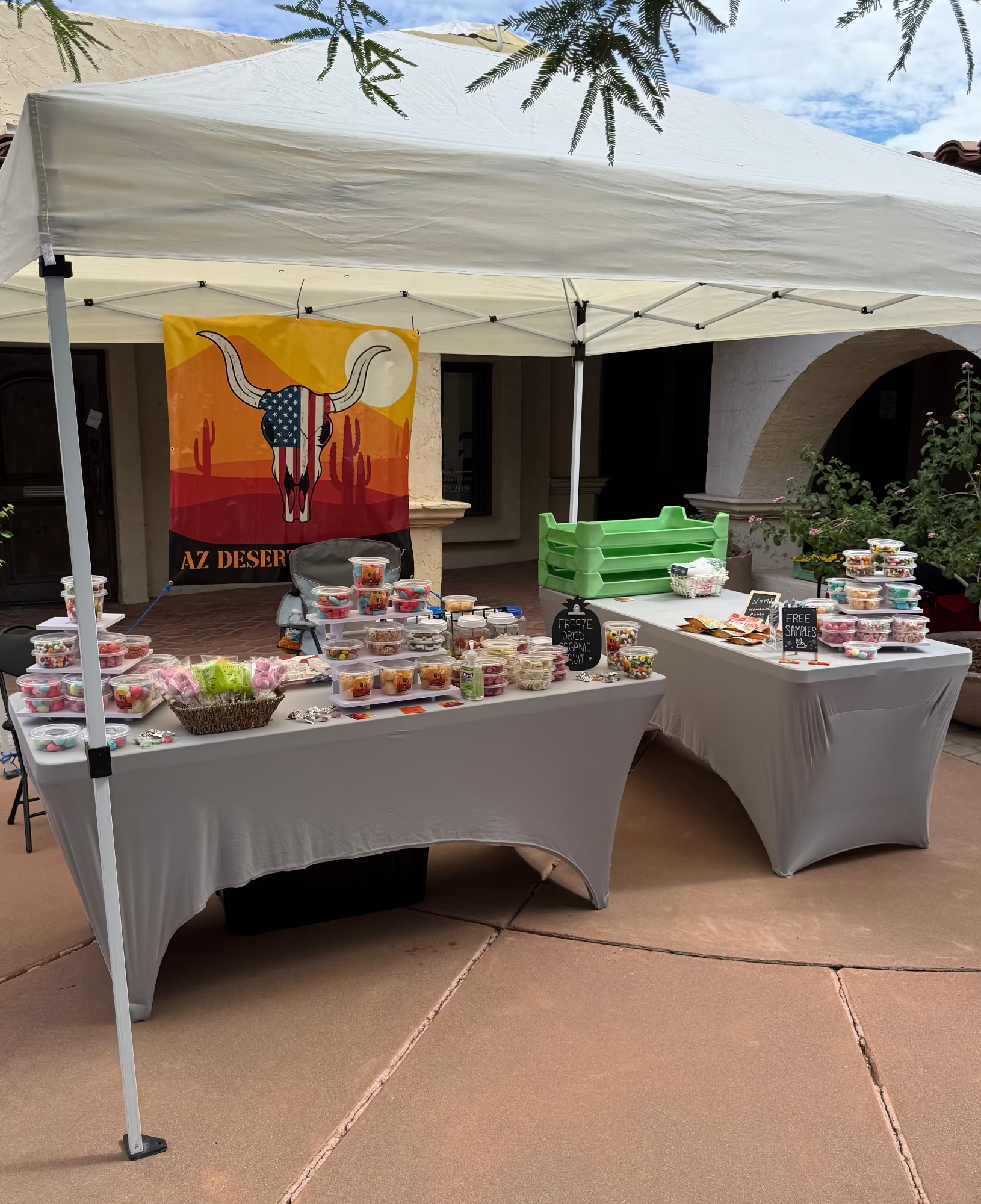Outdoor event with tables under a canopy displaying food and a colorful banner.