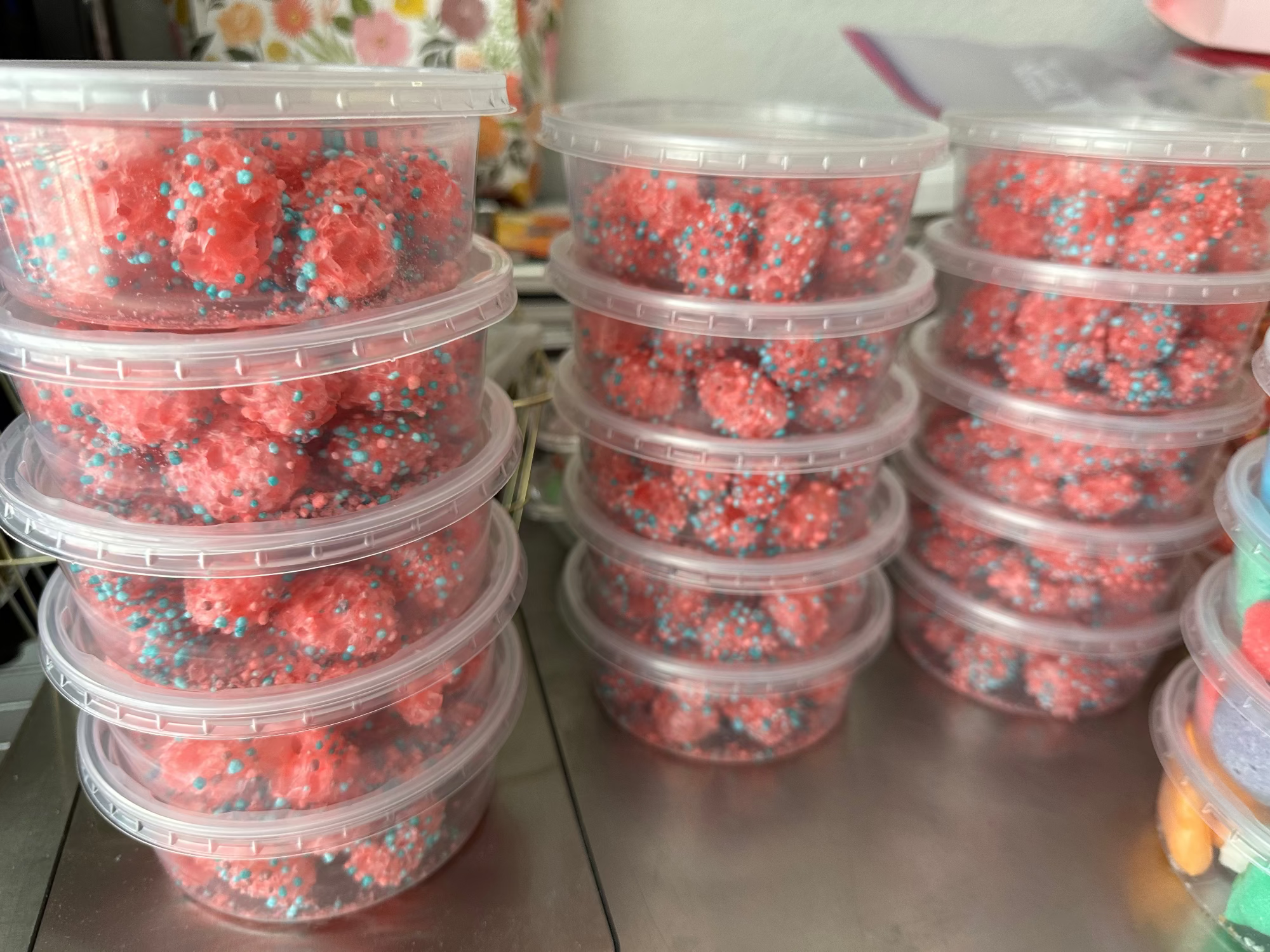Stacks of clear plastic containers filled with freeze dried nerdz gummy clusters on a metal surface.