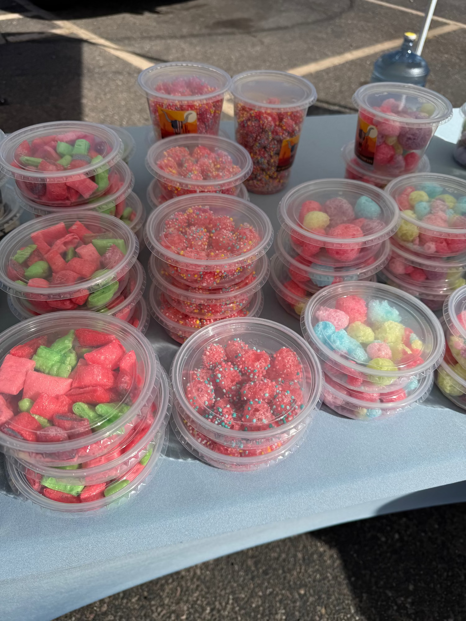 Multiple containers of colorful freeze dried candies on a table outdoors.
